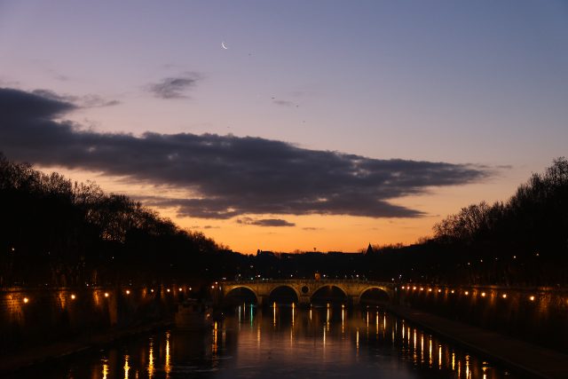The Moon and Venus are shining at dawn above the colorful waters of the Tevere river, in Rome